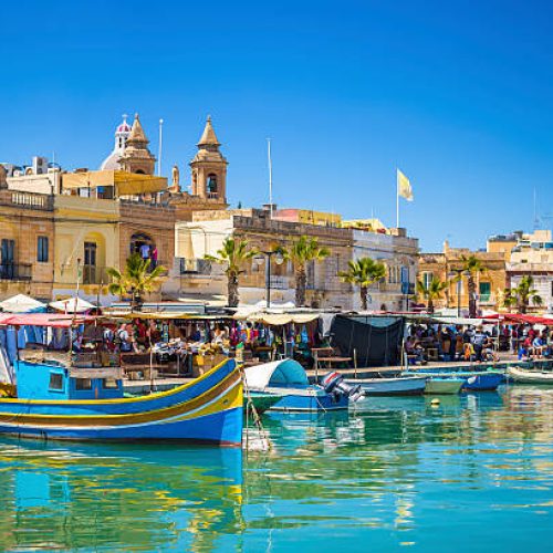 Malta - Marsaxlokk market with traditional Luzzu fishing boats on a beautiful summer day withblue sky and green sea