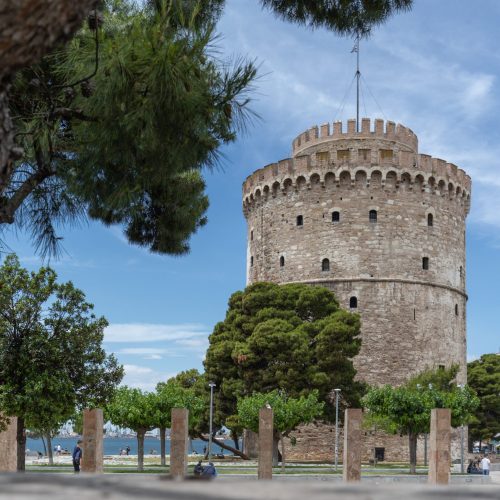 Byzantine heritage White Tower in Thessaloniki with trees in front from under a big pine tree