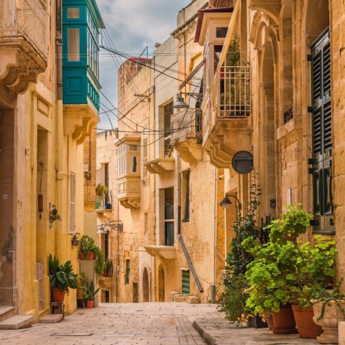 old-medieval-street-with-yellow-buildings-beautiful-balconies-flower-pots-birgu-valletta-malta