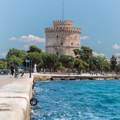 A seafront promenade in Thessaloniki with a Byzantine heritage White Tower behind trees